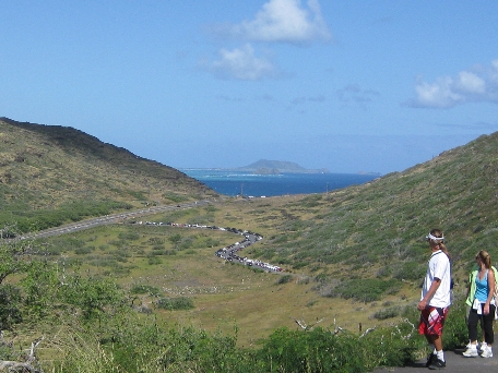 A long line of hikers keep stride in line while walking the path up the side of the hill