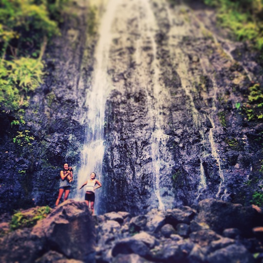 2 girls stand at the bottom of a huge waterfall