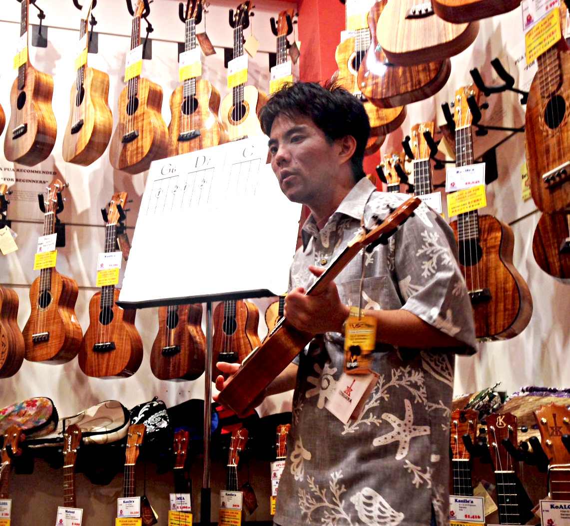 An ukulele teacher standing in front of a wall of ukuleles