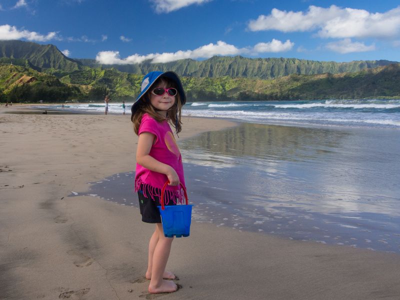 A small girls stands on a beach in Kauai