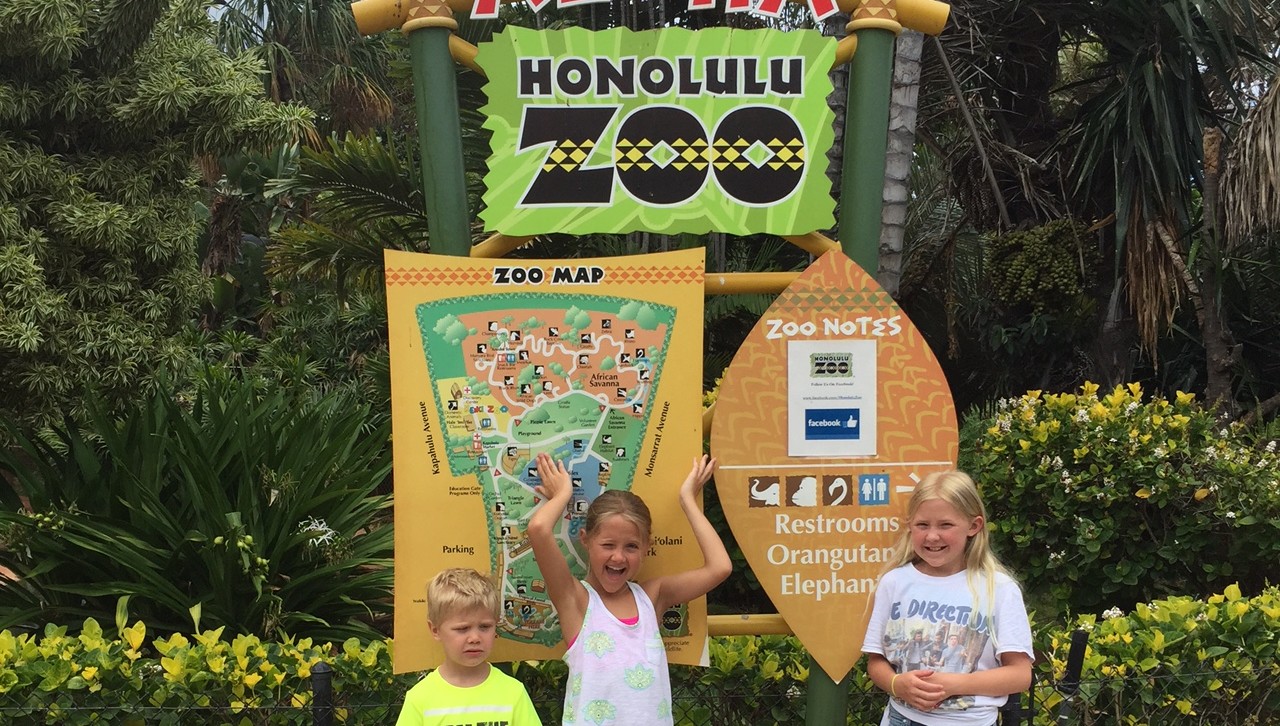 three children standing in front of the honolulu zoo sign