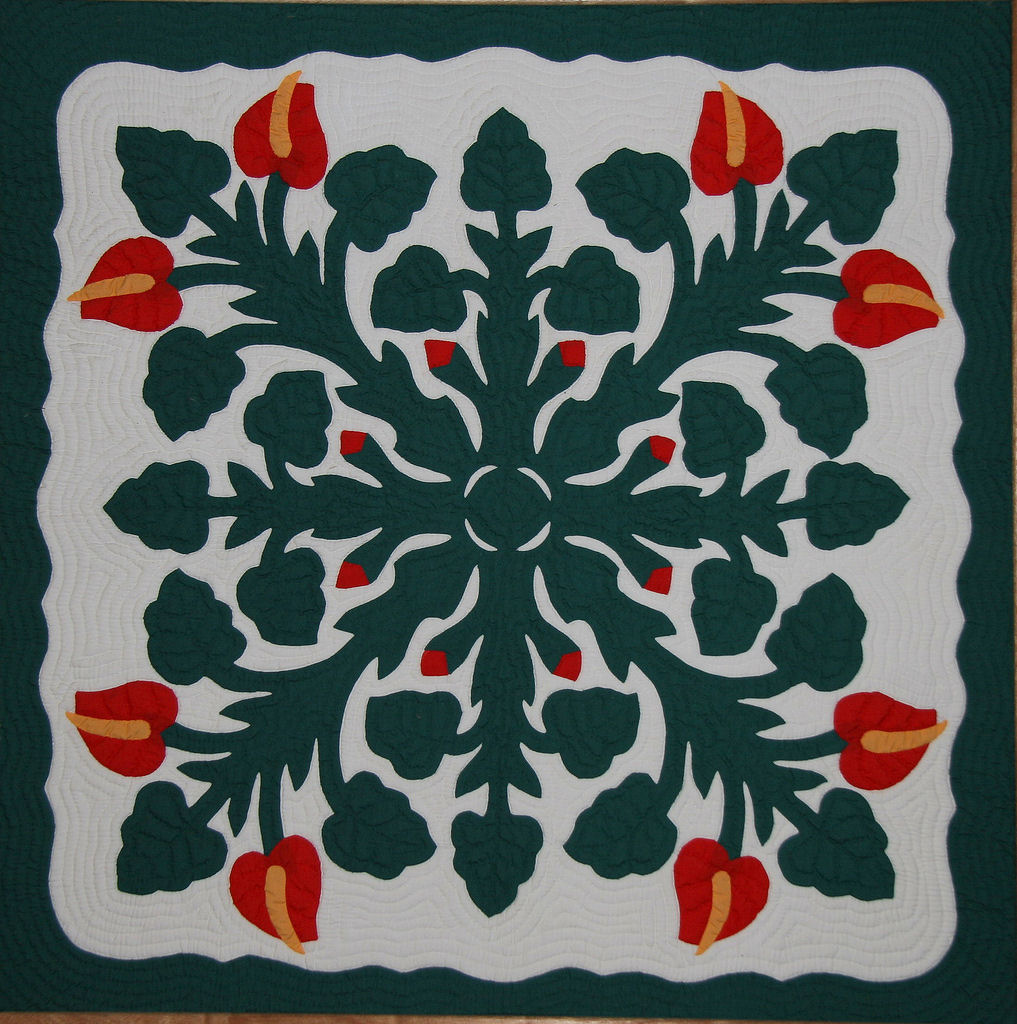 a green and red flower on a hawaiian quilt