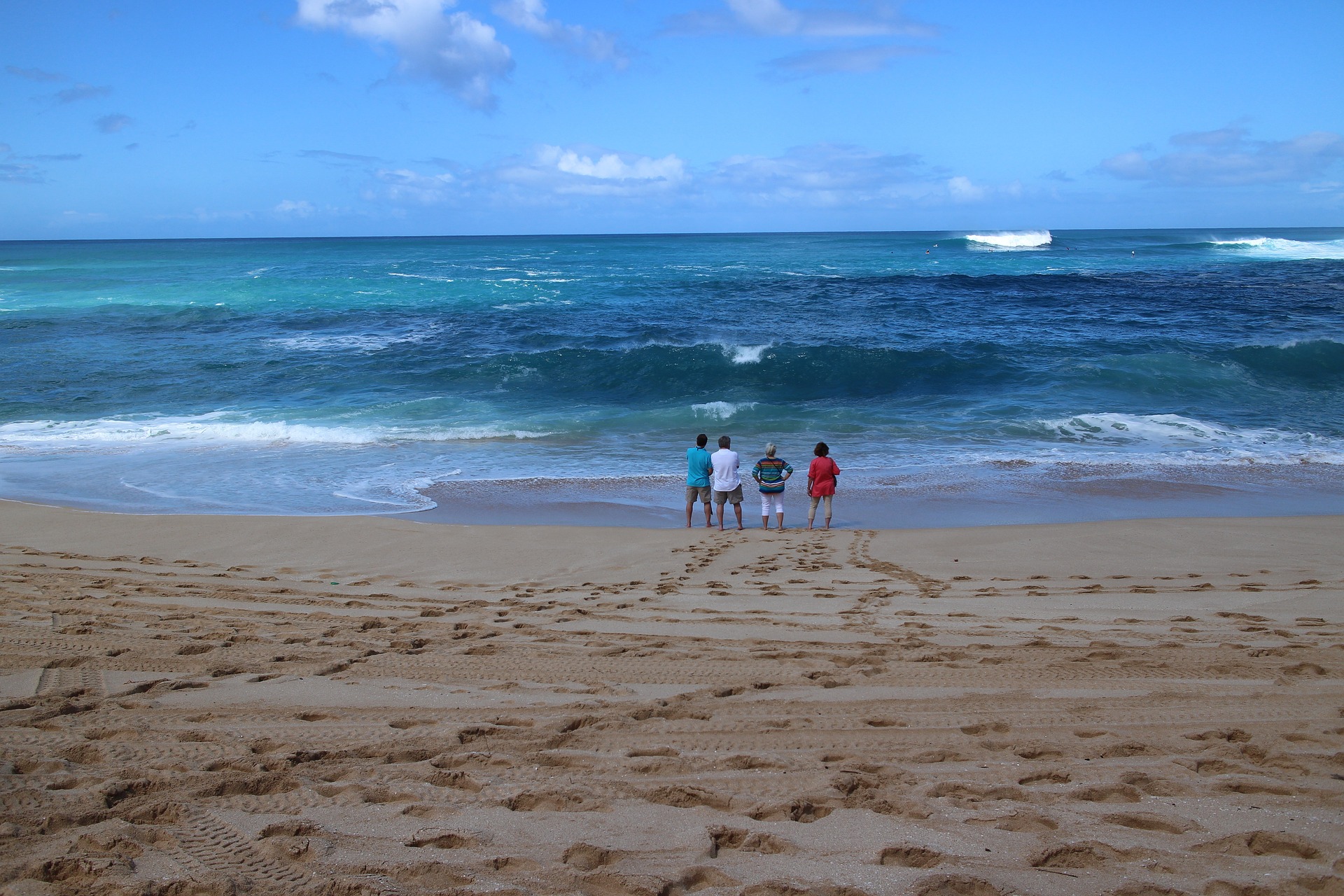 Four men standing on the beach looking at the surf